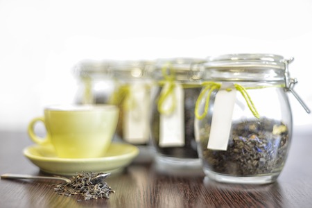 tea in spoon, glass jars and cup on old wooden table with white backgroundの写真素材