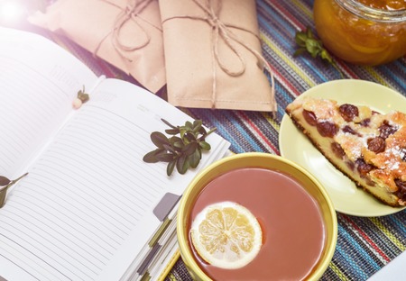 cherry pie, tea, glass jar of honey and other decorations on the colorful tablecloth. sunlight