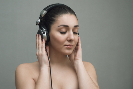 Woman with big headphones and listening to music on a grey backgroundの写真素材