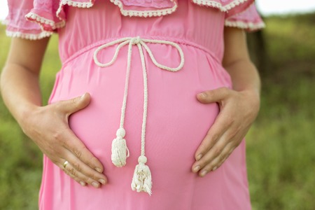 pregnant woman in a pink dress, holding her tummy closeの写真素材