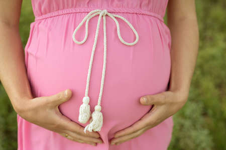 pregnant woman in a pink dress, holding her tummy closeの写真素材
