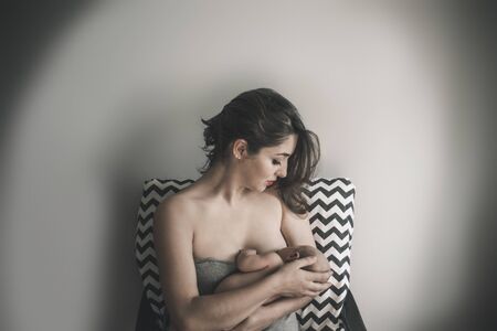 Young mother holding her newborn child. Mom nursing baby. Family at homeの写真素材