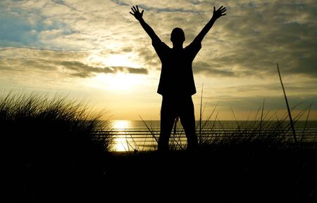 Silhouette man standing in front of sunsetの写真素材