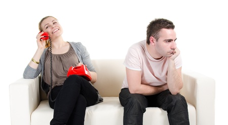 Woman sitting on sofa, talking on phone, man sitting bored next to her - isolated on white backgroundの写真素材