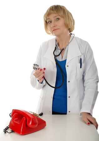 Mature woman doctor with stethoscope standing next to red retro phoneの写真素材