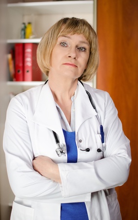 Mature woman doctor in white coat standind in front of shelf with medical filesの写真素材
