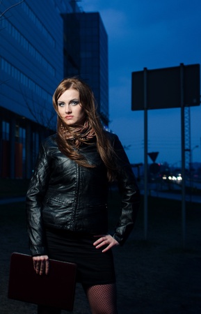Beautiful businesswoman with brown briefcase at night - office building in the backgroundの写真素材