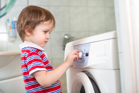 Little baby boy programming washing machine in bathroom - dangerの写真素材