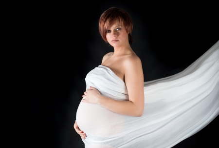 Sexy pregnant woman wrapped in white cloth - isolated on black backgroundの写真素材
