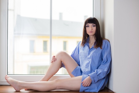 Portrait of beauty brunette sitting on window sill at the morningの写真素材