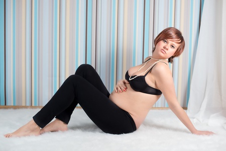 Pregnant woman sitting in bra showing her pregnant bellyの写真素材