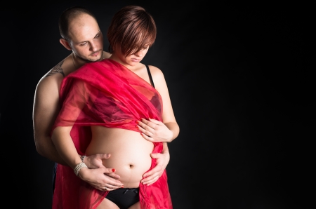 Parents in studio. Pregnant woman in black lingerie wrapped on red fabric の写真素材