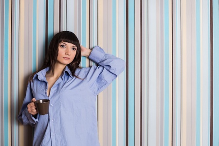 A beautiful young woman in a blue shirt holding a cup of coffeeの写真素材