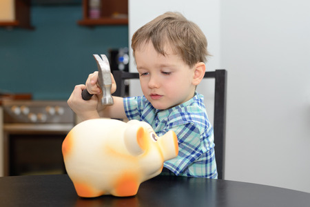 4 year old boy is preparing to break the piggy bank with a hammerの写真素材