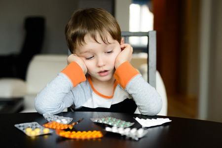 worried 4 year old boy sitting at the table with medications at homeの写真素材