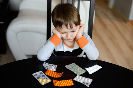sad 4 year old boy sitting at the table with medications at living roomの写真素材