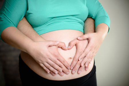 Mom and dad holding hands on the pregnancy belly  They put them in a heart shapeの写真素材