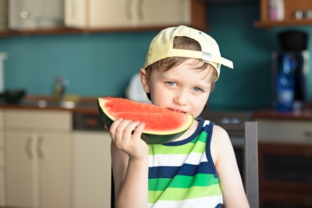 5 year old happy boy eats a watermelon at the kitchen tableの写真素材