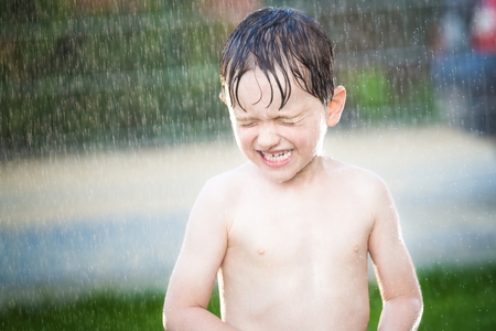 little boy having fun while summer rain at gardenの写真素材