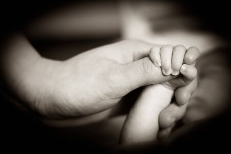 A newborn child is holding the finger of his mother with his little hand.の写真素材