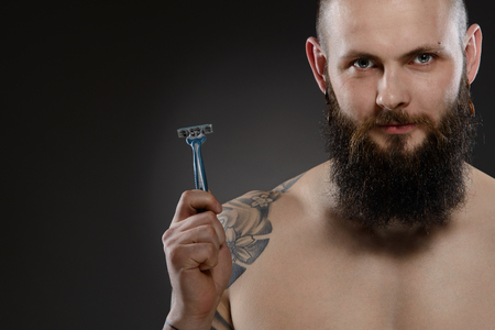 Muscular man with a beard holding a razor - gray backgroundの写真素材