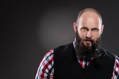 Bearded man in a checkered shirt smoking a pipe on a gray backgroundの写真素材