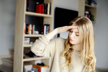 Woman in a home garden touching her head with her hands while having a headache pain and feeling unwell, indoors.の写真素材