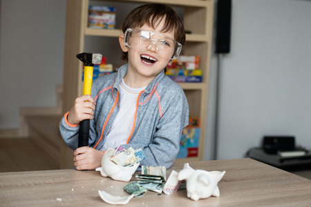 Little boy broke his piggy bank. Smiling, safety glasses on his eyesの写真素材
