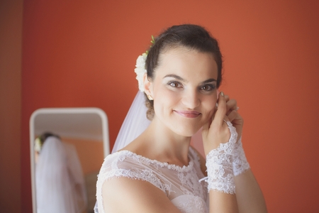 Beautiful bride in white wedding dress puts on earring. Beauty  woman is wearing jewelry. Wedding preparationsの写真素材