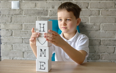 Child playing wooden bricks with letters making word home. Dressed in a white polo shirt