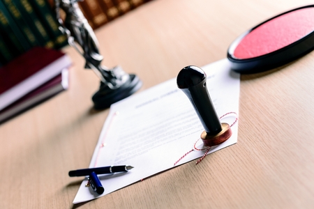 Stamp of notary public on signed document. Pen and Themis with scales of justice in the background.