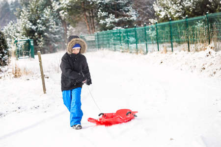 Child pulling red plastic sled. Winter funの写真素材