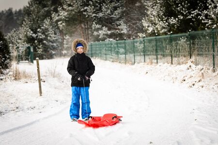 6 years boy pulls his red plastic sled. Winter funの写真素材