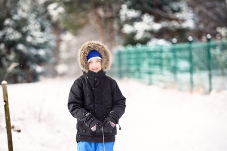 Portrait of cute 6 years boy in winter time. The boy is wearing a black jacket and blue capの写真素材