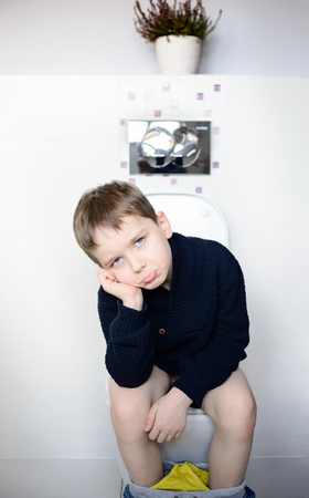 Sad boy sitting on the toilet. Dressed in a dark navy blue woolen sweaterの写真素材