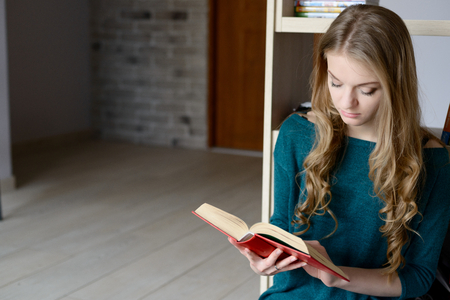 The woman sitting next to bookshelves and reading a bookの写真素材