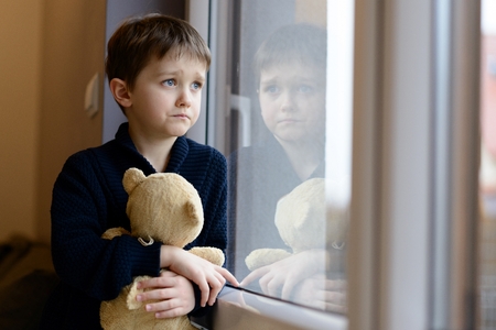 The little boy looks out the window. Rainy Day. Loneliness and waiting conceptの写真素材