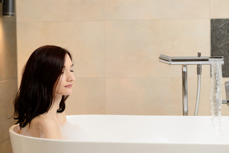 Young attractive brunette taking bath. Relaxed, eyes closed. Woman in bathroomの写真素材