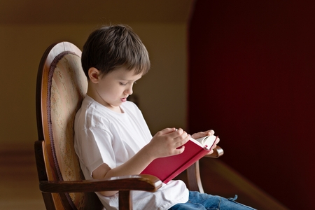 Little boy sitting on old armchair and reading a bookの写真素材