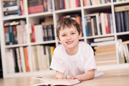 Smiling child reading a book at home. Dressed in a white t shirt and blue jeans. Looking at camera.の写真素材