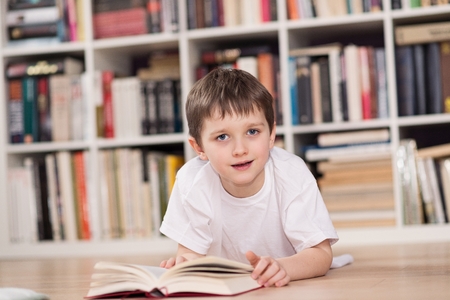 Happy little boy reading a book at home. Dressed in a white t shirt and blue jeans. Looking at camera.の写真素材