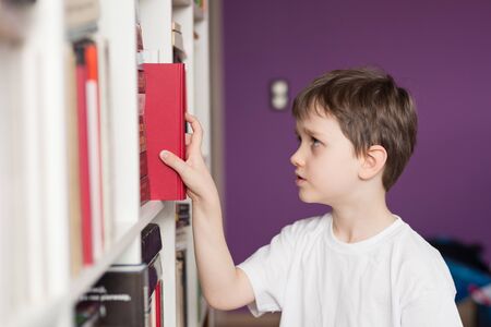 Little boy selecting book from library. Dressed in a white t shirtの写真素材
