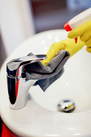 Female hands with rubber gloves spraying liquid detergent on tap and cleaning it with cloth. Spring cleaningの写真素材