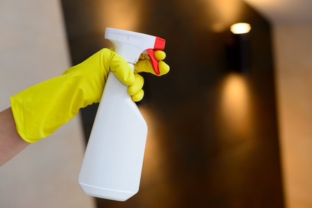 Hand with yellow rubber gloves holding white detergent spray bottleの写真素材