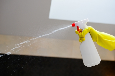 hand with yellow rubber gloves holding white detergent spray bottle and spraying in bathroomの写真素材
