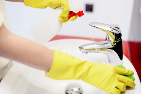 Female hands with rubber gloves spraying liquid detergent on tap and cleaning it with sponge. Spring cleaningの写真素材