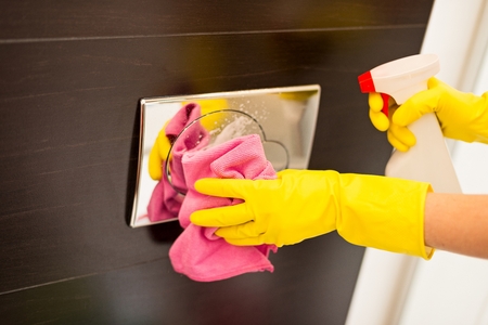 Female hands with yellow rubber protective gloves cleaning flush button in toilet. Spring cleaningの写真素材