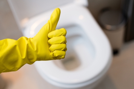 Close up of female hand with yellow protective rubber glove showing thumb up ok sign against clean toilet. Spring cleaningの写真素材