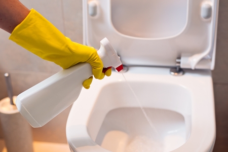 Close up of female hand with yellow protective rubber glove cleaning toilet with spray antibacterial detergent . Spring cleaningの写真素材