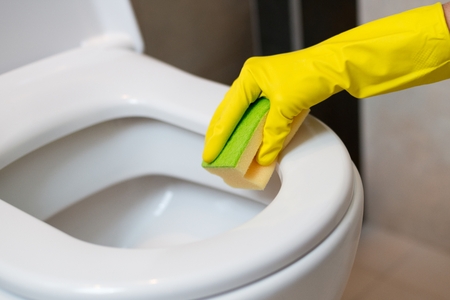 Female hands with yellow rubber gloves cleaning toilet in wc with yellow sponge. Spring cleaningの写真素材